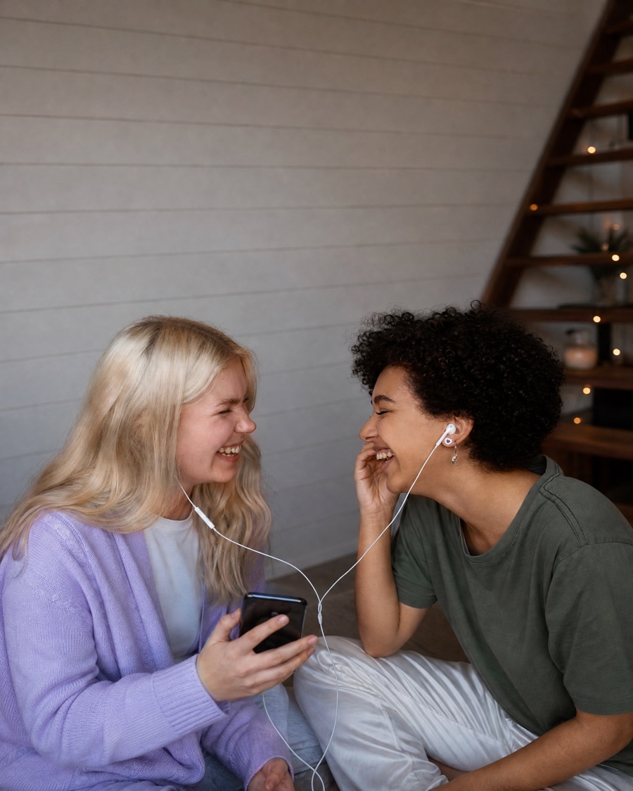 Two best friends sharing a pair of earphones, laughing