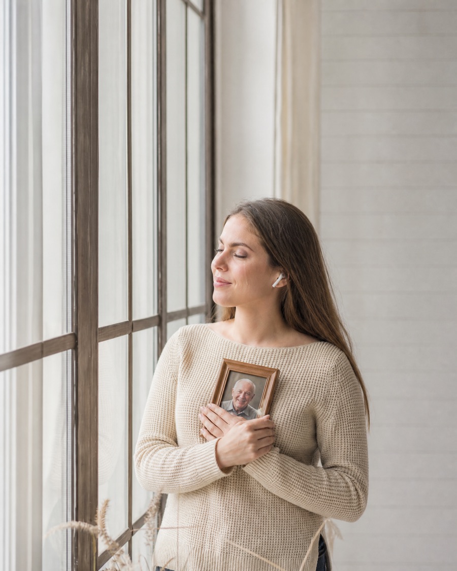 A young woman with earbuds in, holding a photo of her grandfather